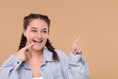 Smiling woman with braces pointing at something on beige background. Space for text