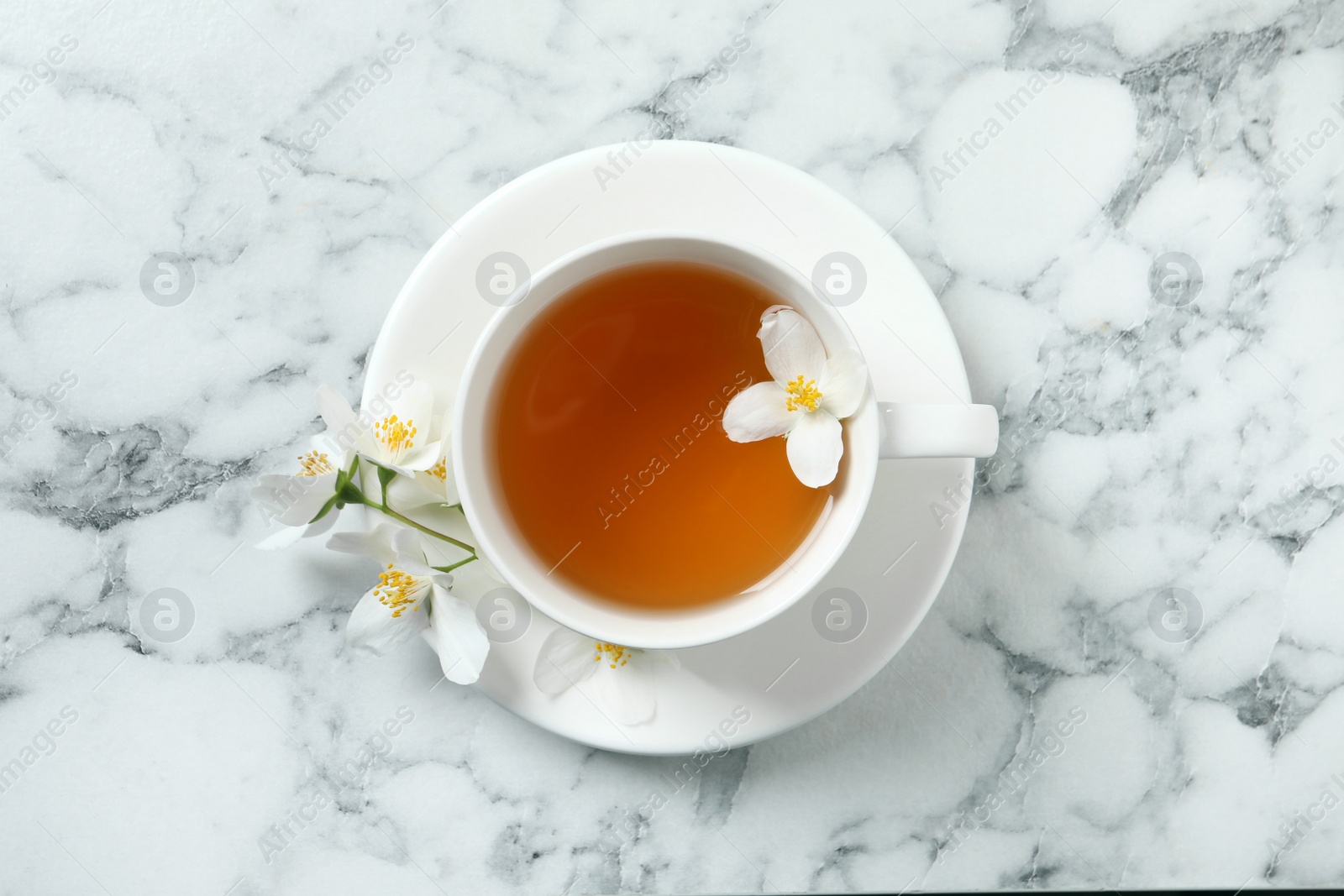 Photo of Cup of aromatic jasmine tea and fresh flowers on white marble table, top view