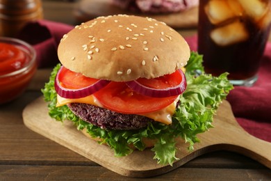 Tasty vegetarian burger with beet patty, sauce and soda drink on wooden table, closeup