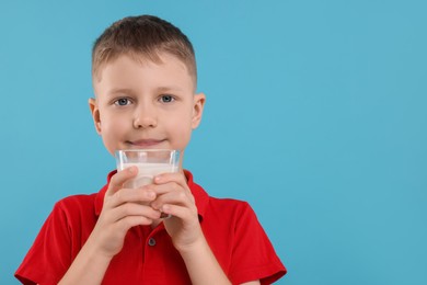 Cute boy with glass of fresh milk on light blue background, space for text