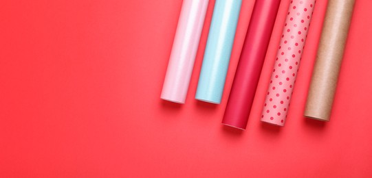 Photo of Rolls of colorful wrapping papers on red background, flat lay. Space for text