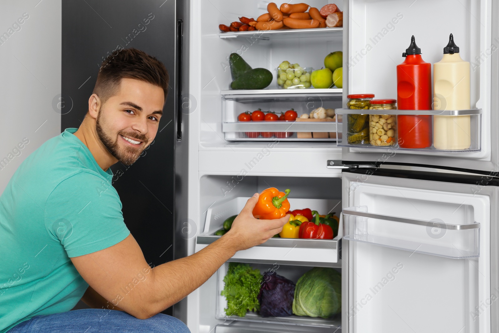 Photo of Young man taking bell pepper out of refrigerator indoors