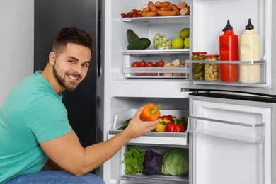 Photo of Young man taking bell pepper out of refrigerator indoors