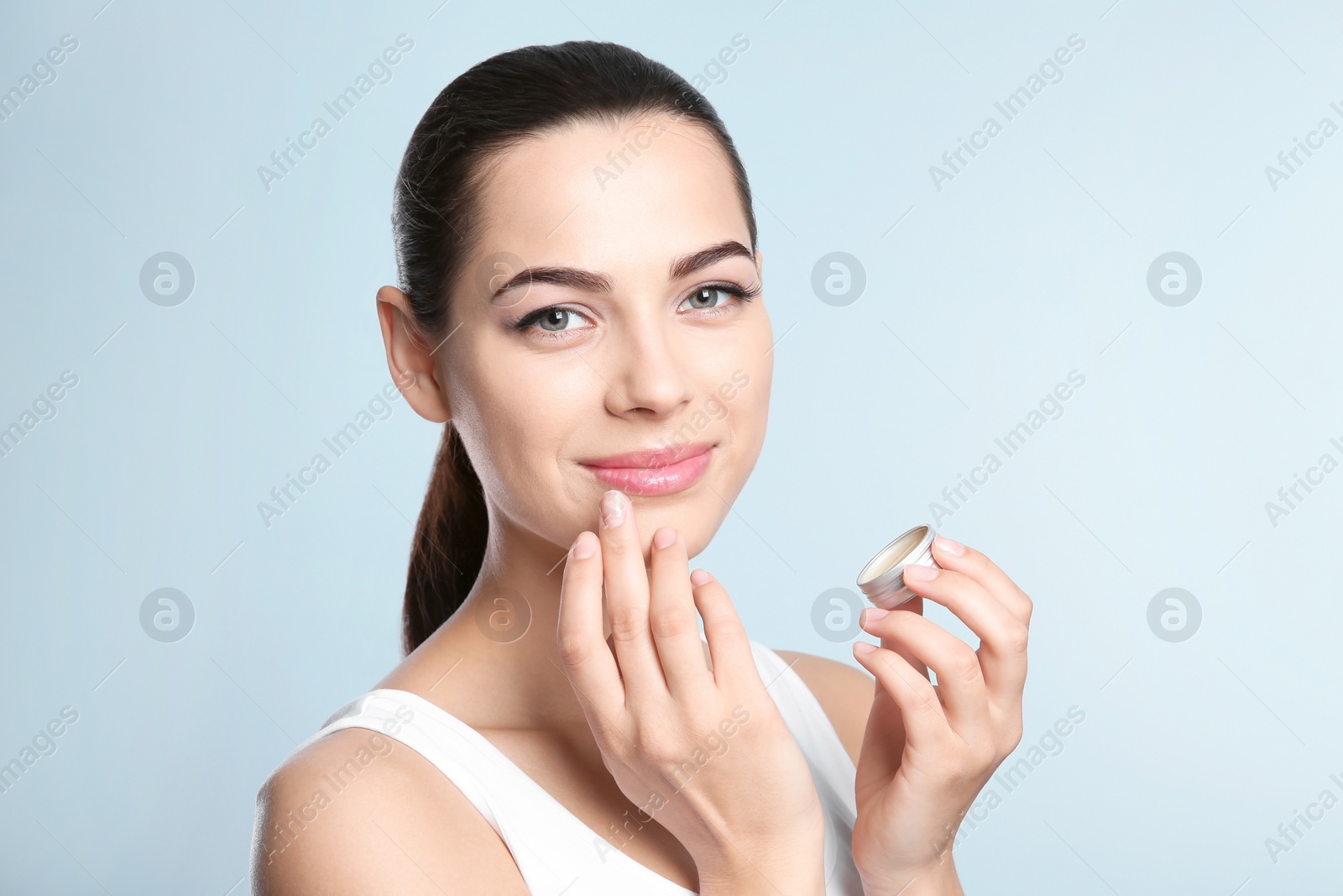 Photo of Young woman applying balm on her lips against color background