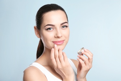 Young woman applying balm on her lips against color background