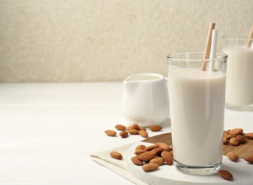Photo of Glasses of almond milk and almonds on white wooden table, space for text