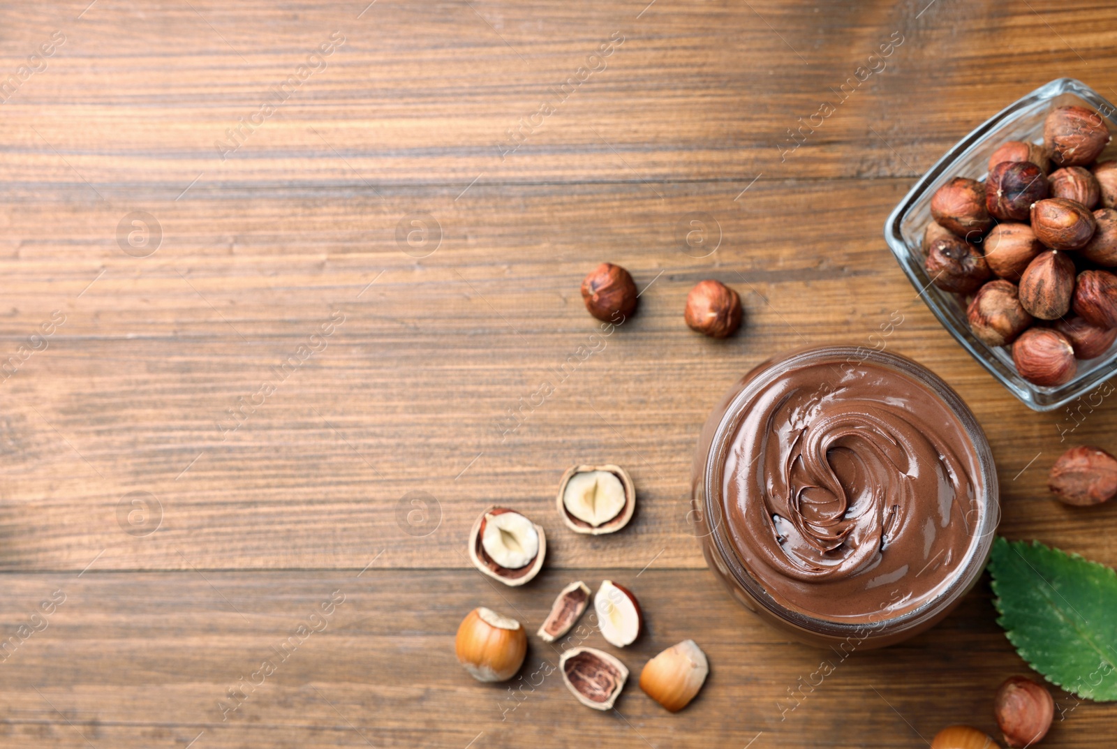 Photo of Flat lay composition with tasty chocolate hazelnut spread on wooden table, space for text