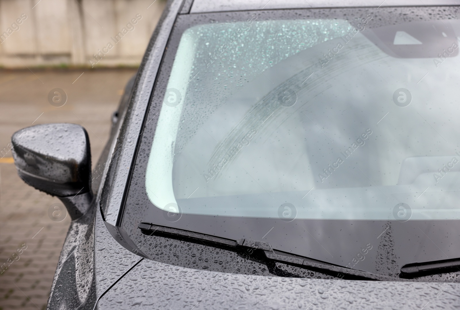 Photo of Car wipers cleaning water drops from windshield glass outdoors, closeup