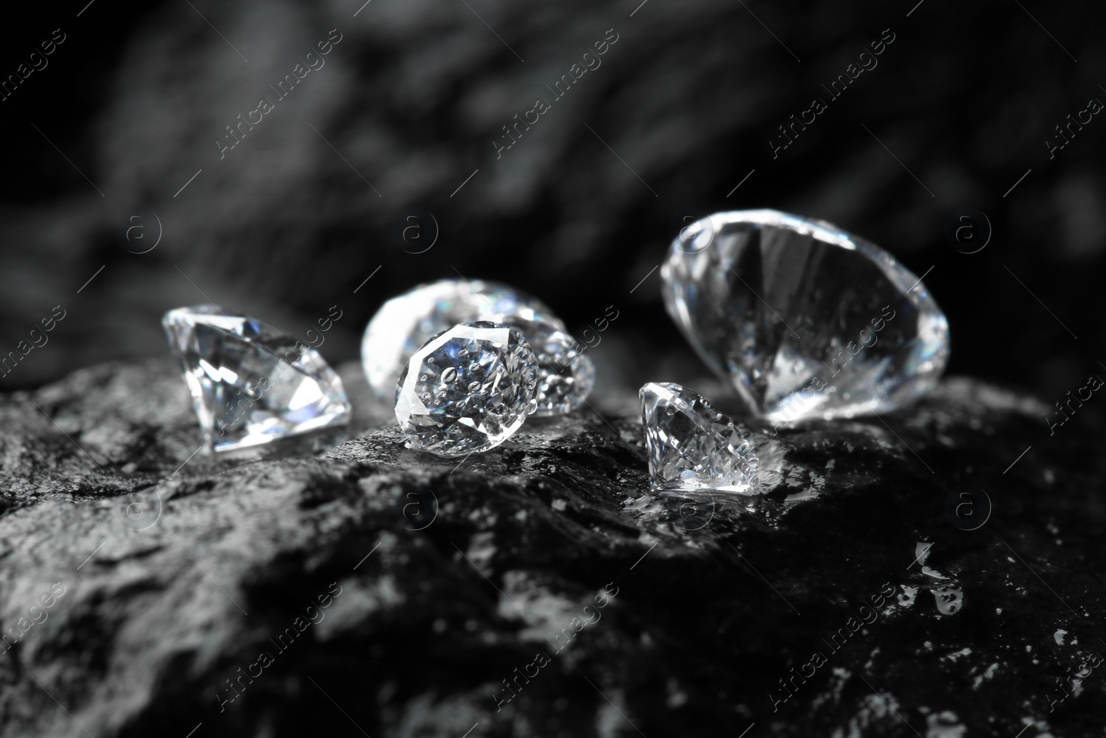 Photo of Different shiny diamonds on wet stone surface, closeup