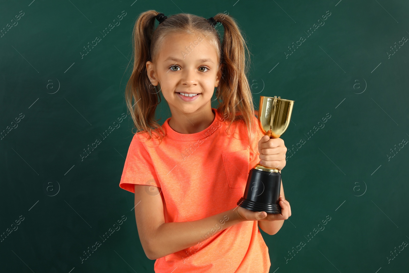 Photo of Happy girl with golden winning cup near chalkboard