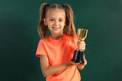 Photo of Happy girl with golden winning cup near chalkboard