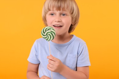 Happy little boy with lollipop swirl on orange background