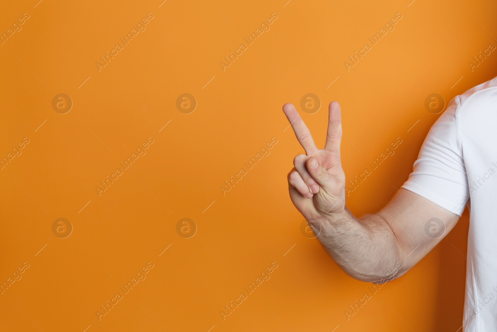 Photo of Young man showing victory gesture on color background. Space for text