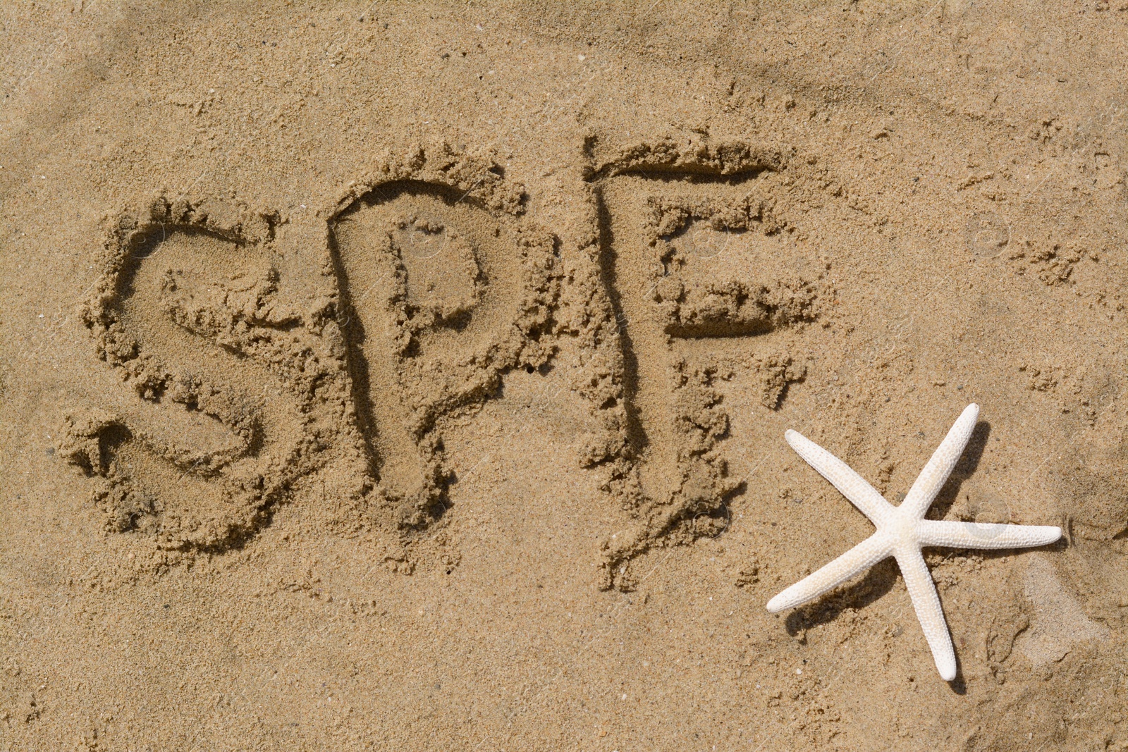 Photo of Abbreviation SPF written on sand and starfish at beach, top view