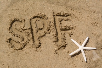 Photo of Abbreviation SPF written on sand and starfish at beach, top view