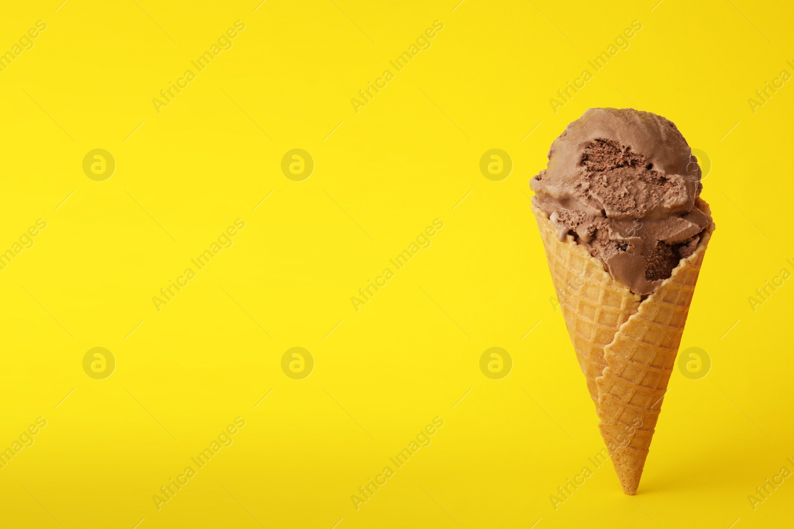 Photo of Delicious chocolate ice cream in waffle cone on yellow background. Space for text