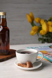 Cup of aromatic coffee, caramel candies and syrup on white wooden table