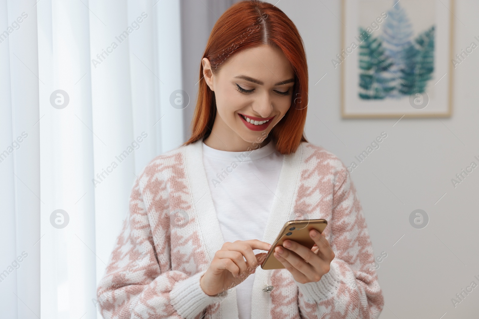 Photo of Happy woman sending message via smartphone at home