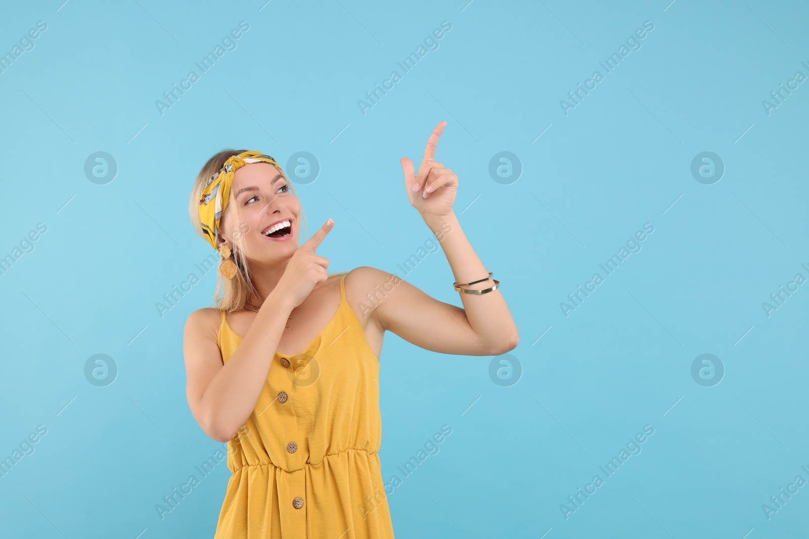 Photo of Portrait of happy hippie woman pointing at something on light blue background. Space for text