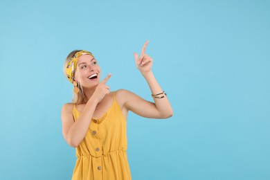 Photo of Portrait of happy hippie woman pointing at something on light blue background. Space for text