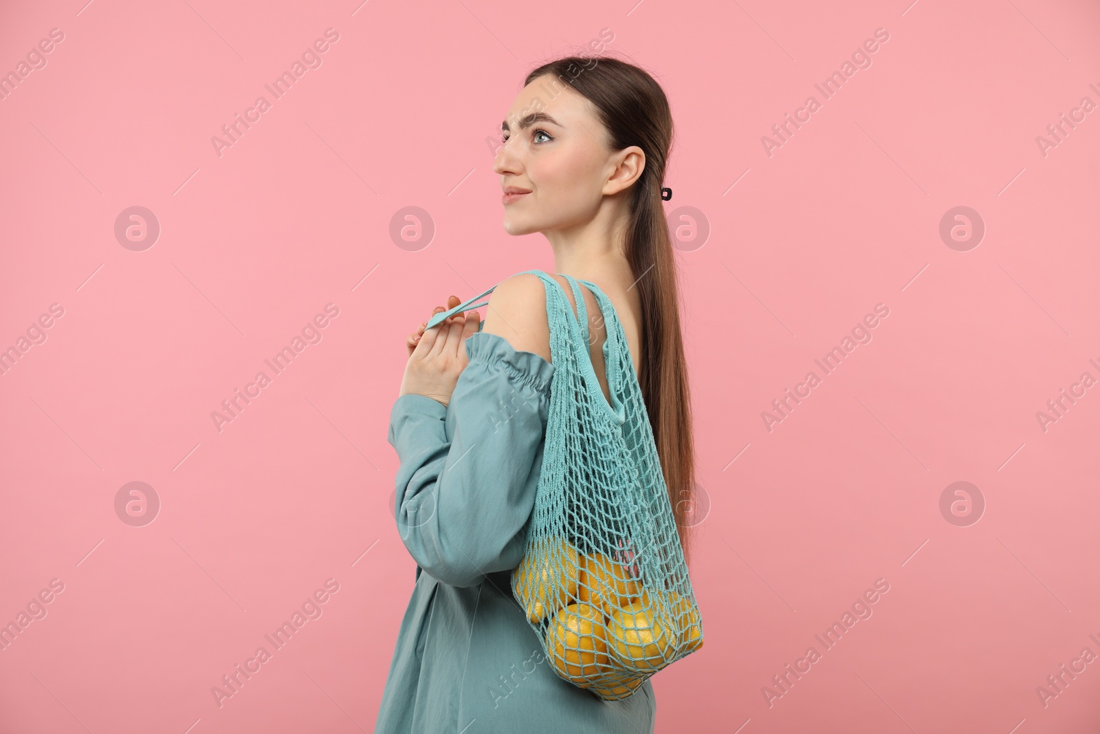 Photo of Woman with string bag of fresh lemons on pink background