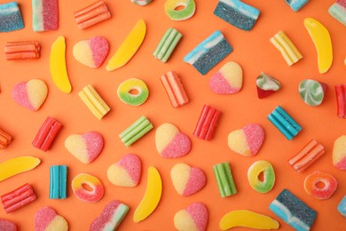 Photo of Many different jelly candies on orange background, flat lay