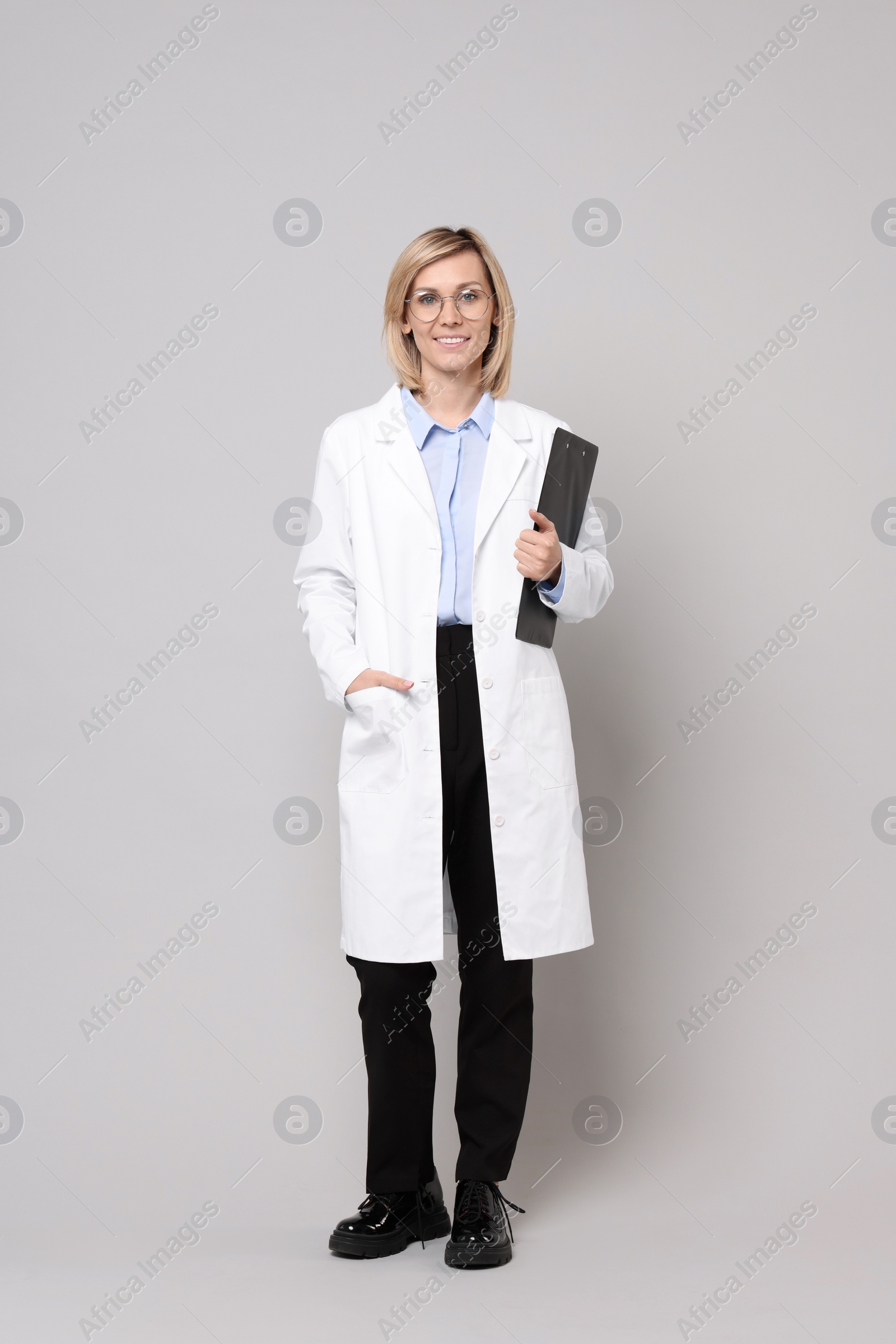 Photo of Smiling doctor with clipboard on grey background