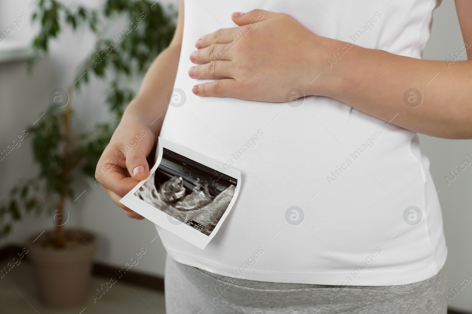 Photo of Pregnant woman with ultrasound picture of baby in room, closeup