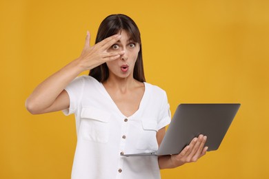Photo of Embarrassed woman with laptop covering face on orange background