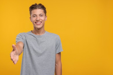 Photo of Happy man welcoming and offering handshake on orange background. Space for text