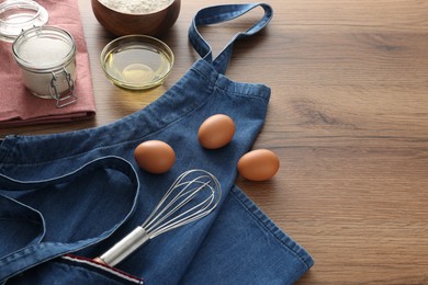 Photo of Denim apron with kitchen tool and different ingredients on wooden table, space for text