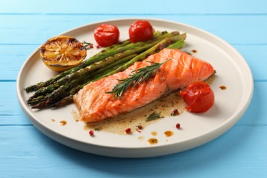 Tasty grilled salmon with tomatoes, asparagus and spices on light blue wooden table, closeup