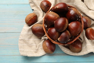 Photo of Wicker bowl with roasted edible sweet chestnuts on light blue wooden table, flat lay