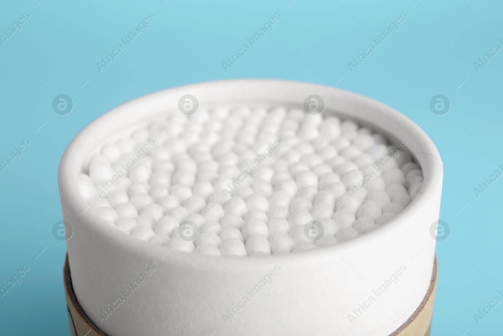 Photo of Container with new cotton buds on light blue background, closeup