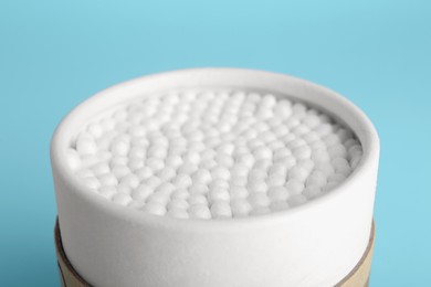 Photo of Container with new cotton buds on light blue background, closeup