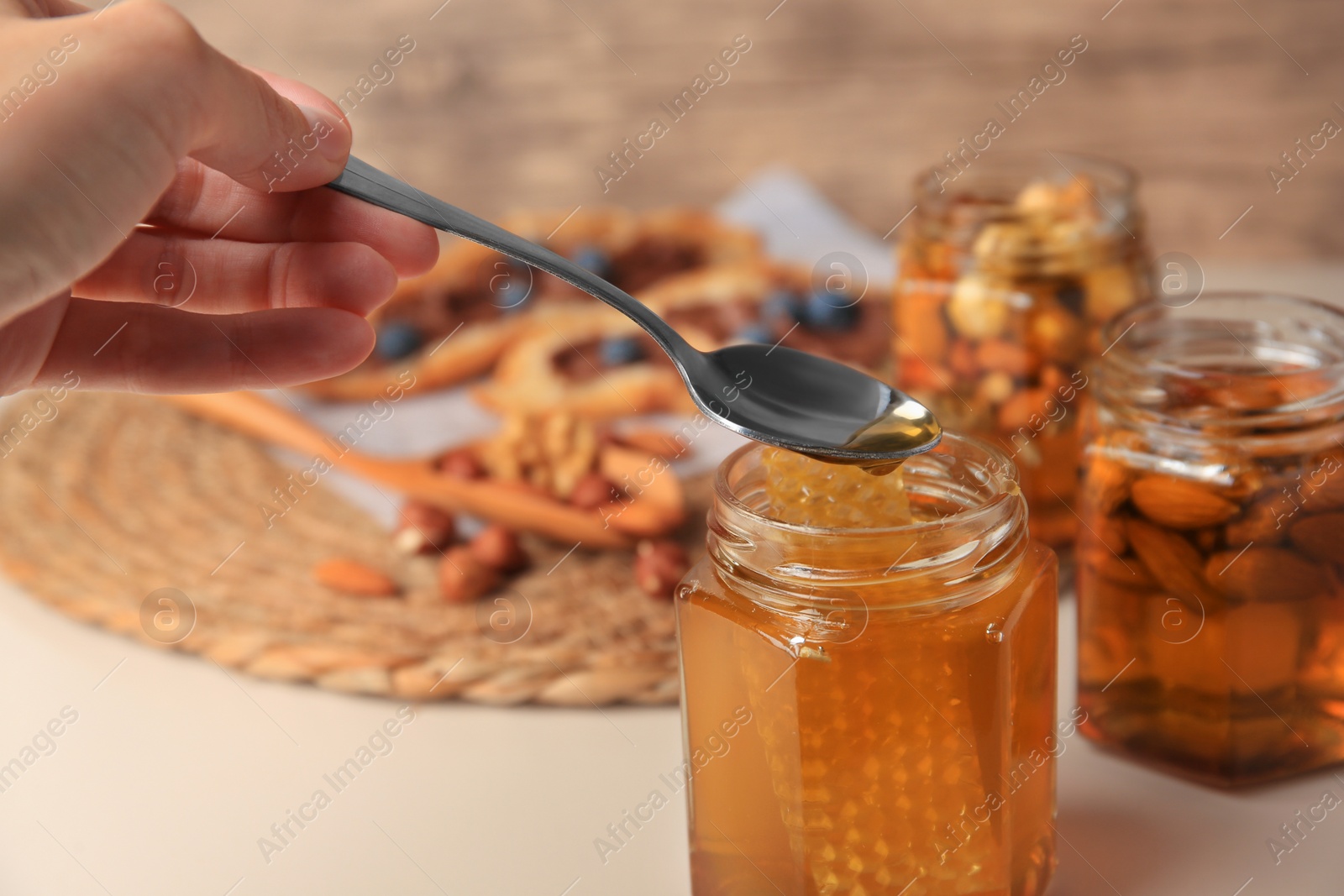 Photo of Woman taking spoon of honey from glass jar at beige table, closeup