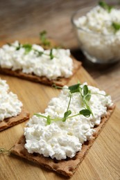 Photo of Crispy crackers with cottage cheese and microgreens on wooden board, closeup