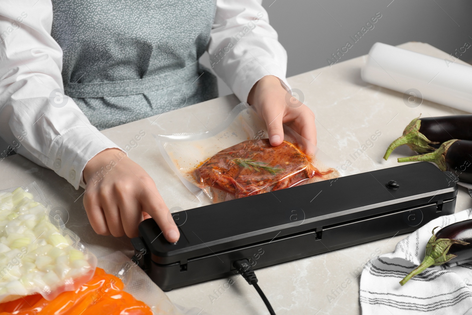 Photo of Woman using sealer for vacuum packing on white marble table, closeup