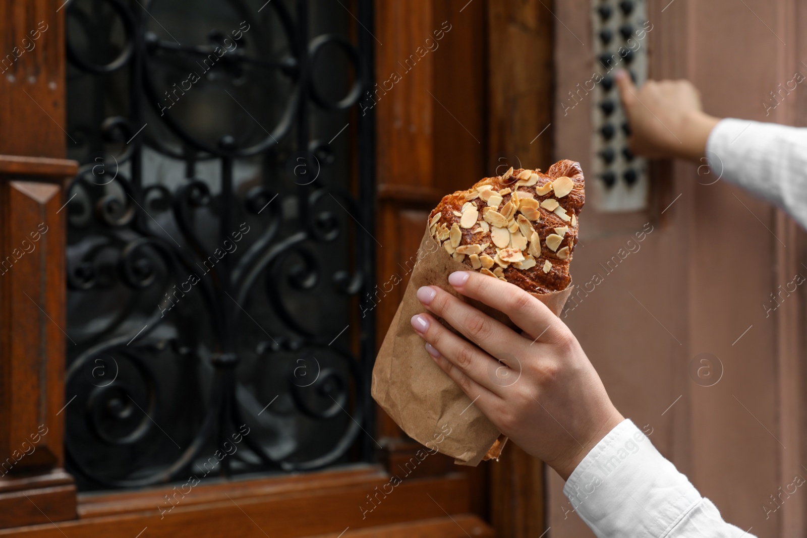 Photo of Woman holding delicious croissant and ringing doorbell outdoors, closeup. Space for text