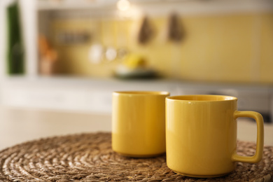 Photo of Yellow cups on wicker mat in kitchen. Space for text