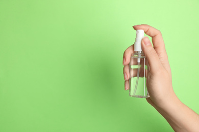 Photo of Woman holding antiseptic spray on green background, closeup. Space for text