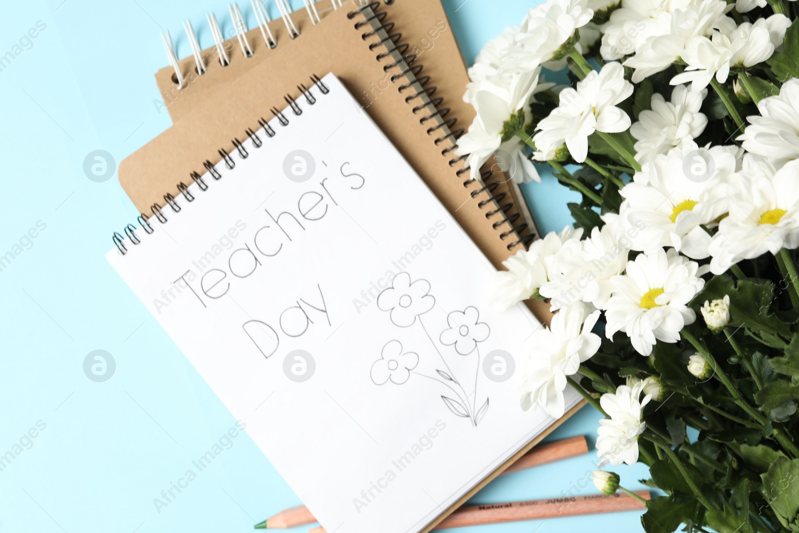 Photo of Notebook with phrase Teacher's Day and beautiful white flowers on light blue background, flat lay