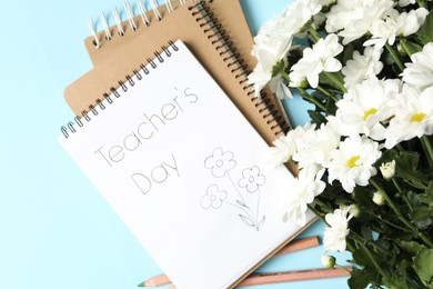 Photo of Notebook with phrase Teacher's Day and beautiful white flowers on light blue background, flat lay