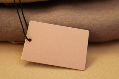 Photo of Garment with cardboard tag on kraft paper sheet, closeup. Space for text