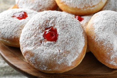 Photo of Delicious donuts with jelly and powdered sugar on wooden pastry stand, closeup