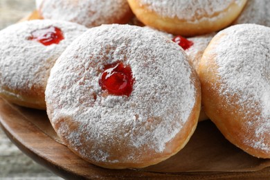 Delicious donuts with jelly and powdered sugar on wooden pastry stand, closeup