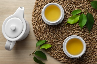 Photo of Green tea in white cups with leaves and teapot on wooden table, flat lay