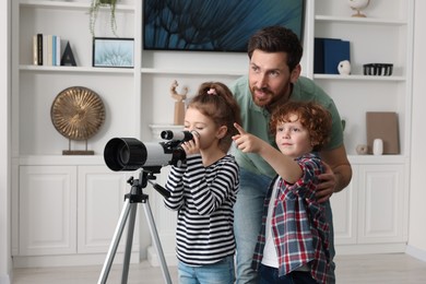 Photo of Happy father and children looking at stars through telescope in room