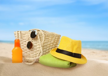 Stylish bag with different accessories on sandy beach near ocean