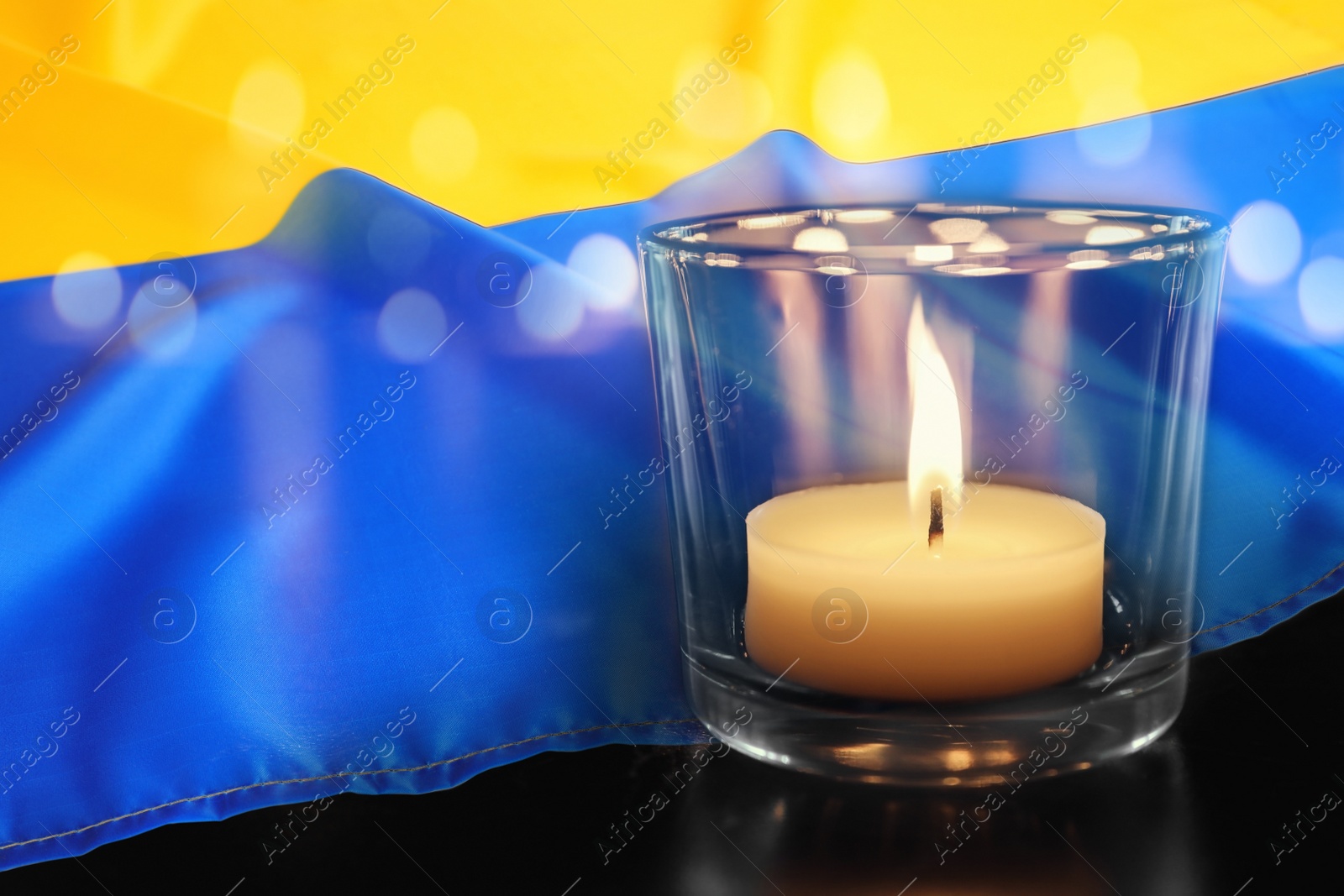 Image of Burning candle and Ukrainian national flag on black table, closeup view